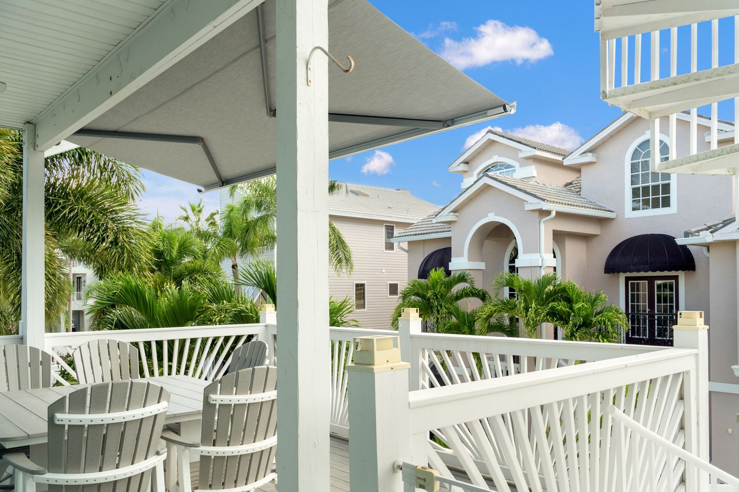 White coastal-style patio with fan-back chairs overlooking tropical landscaping.