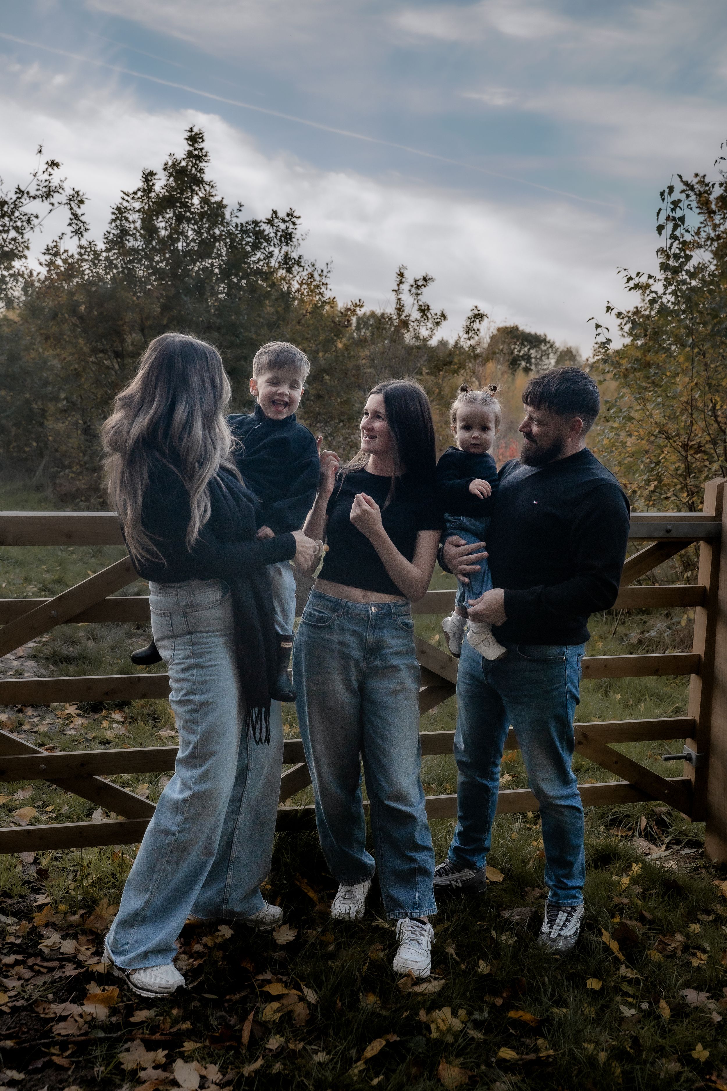 A family in casual clothing stands together on a wooden deck surrounded by autumn foliage at sunset.