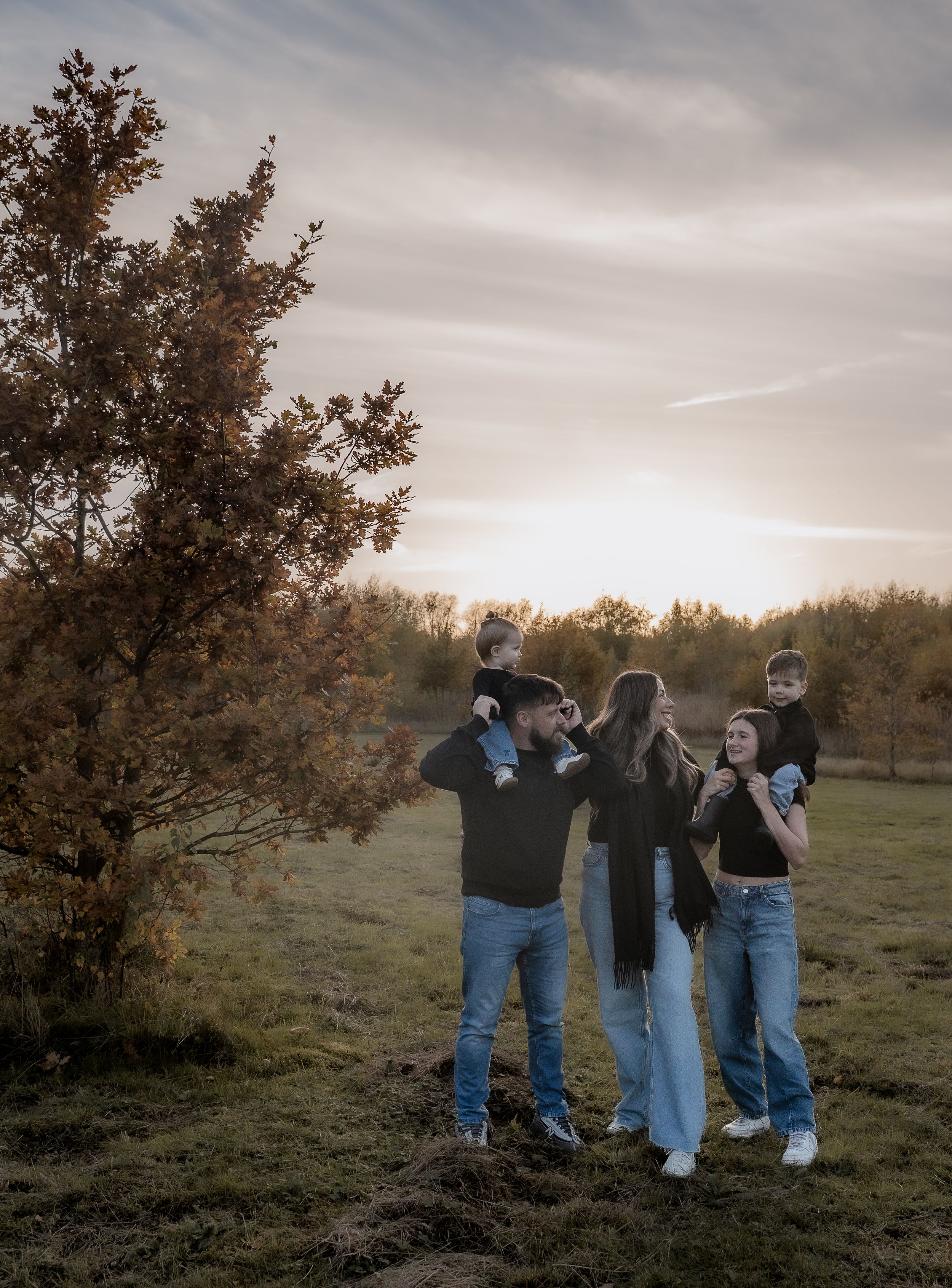 Group of people walking together on a grassy hillside at sunset with autumn trees in the background.