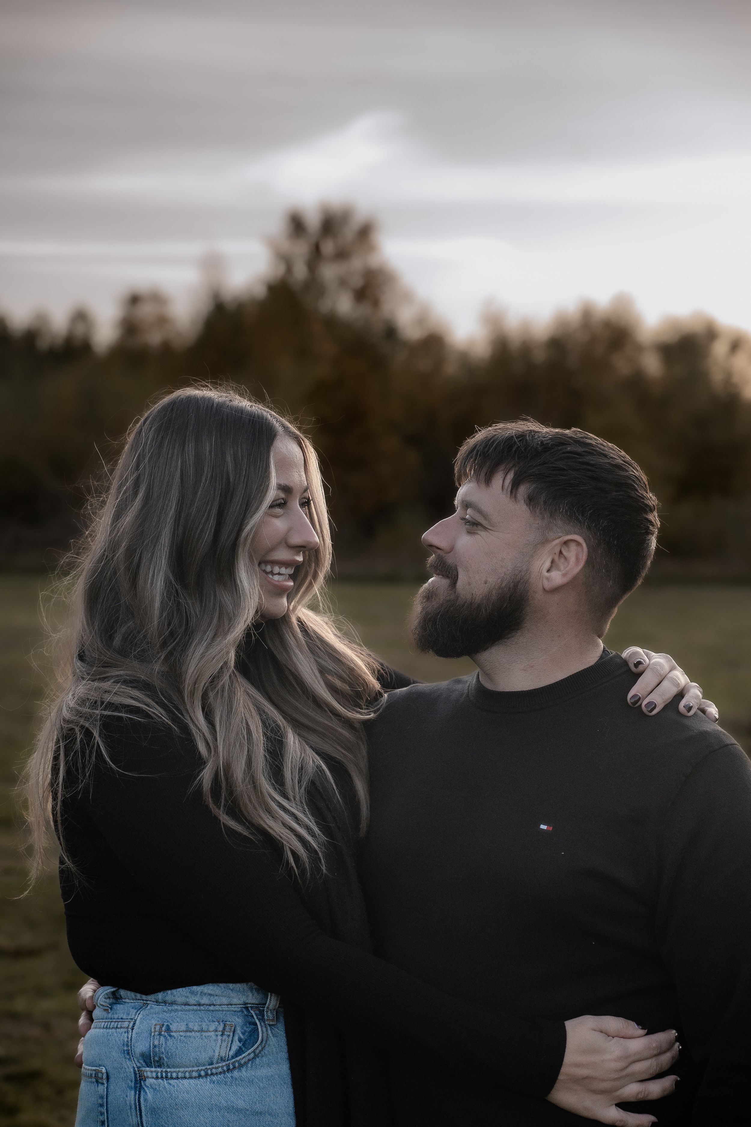 A couple shares intimate moments and laughter together during a moody outdoor photoshoot at sunset.