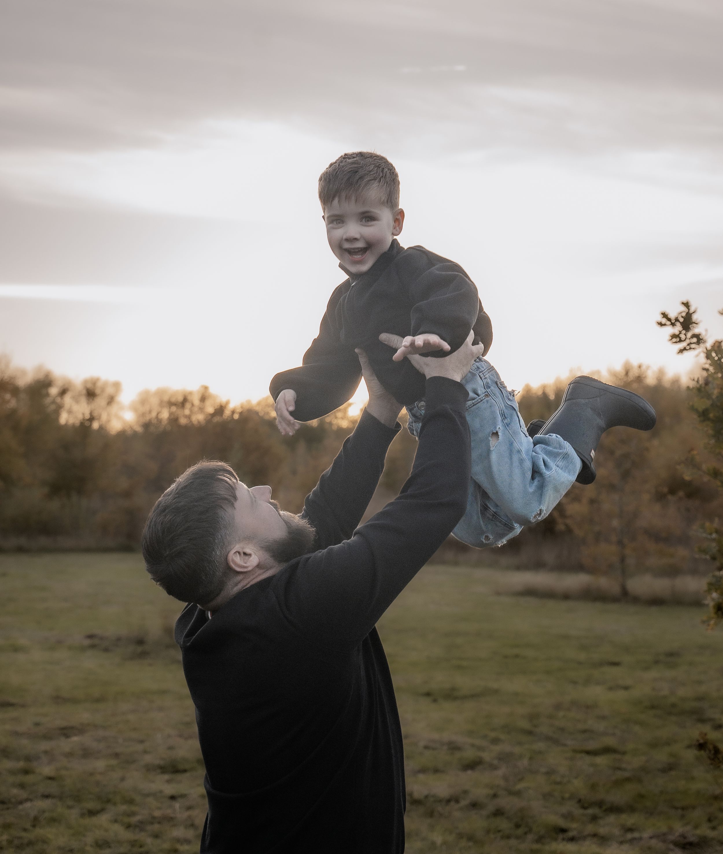 A parent lifts and plays with a small child in a field at sunset, creating a joyful silhouette against the sky.