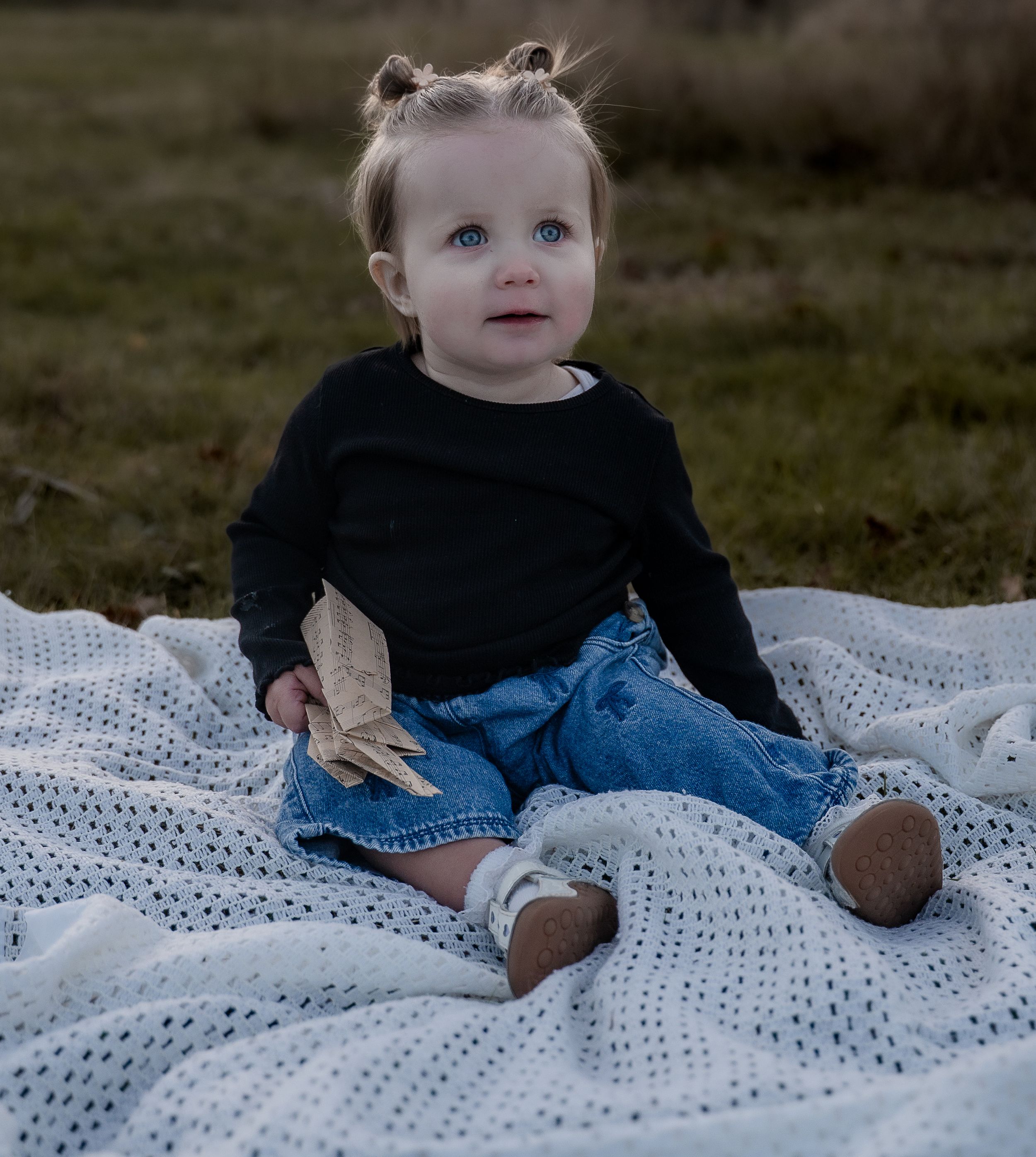 Baby in blue jeans sits on white crochet blanket outdoors during milestone photo session.