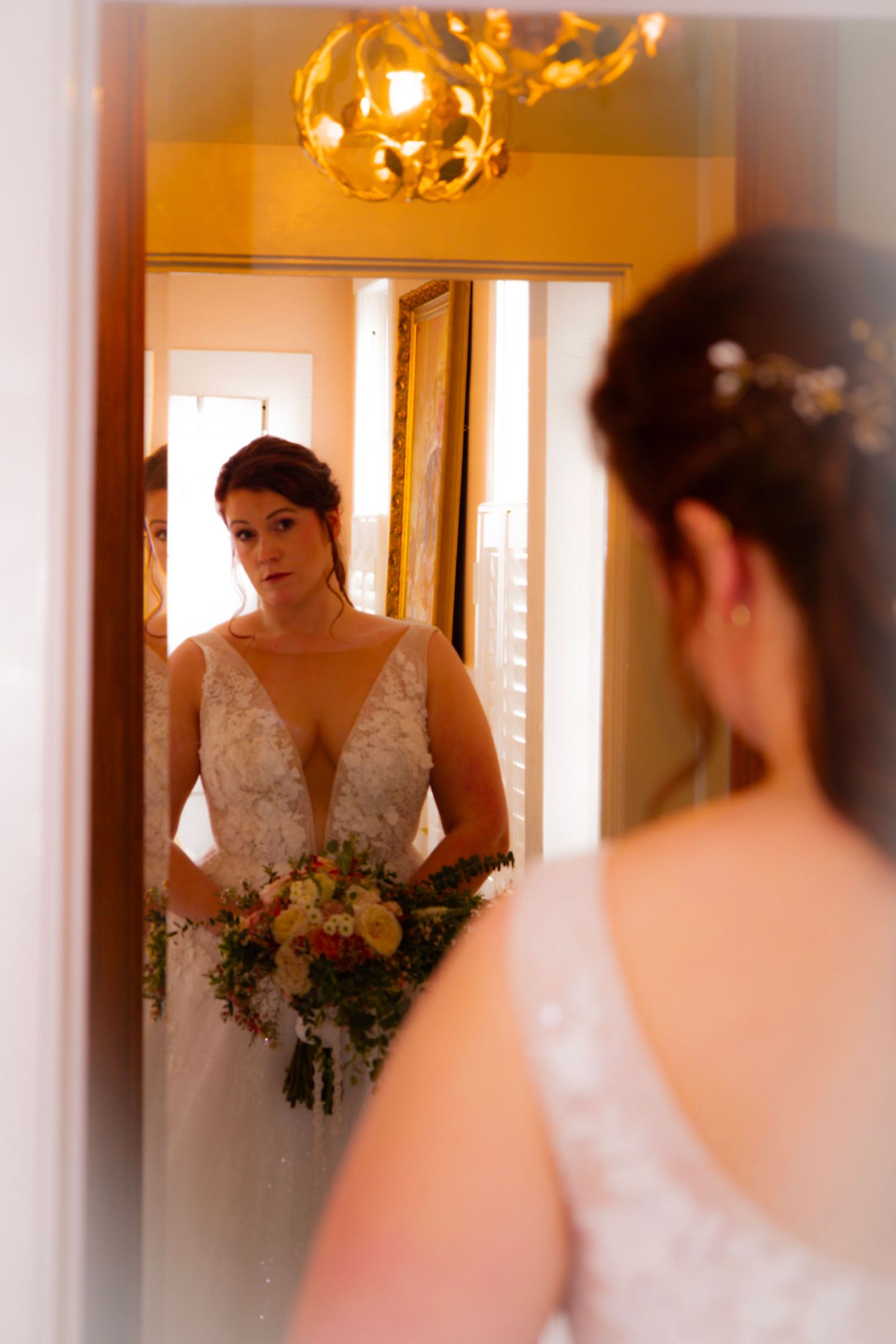 Romantic wedding couple embraces under elegant crystal chandeliers in rustic wooden barn venue at dusk.