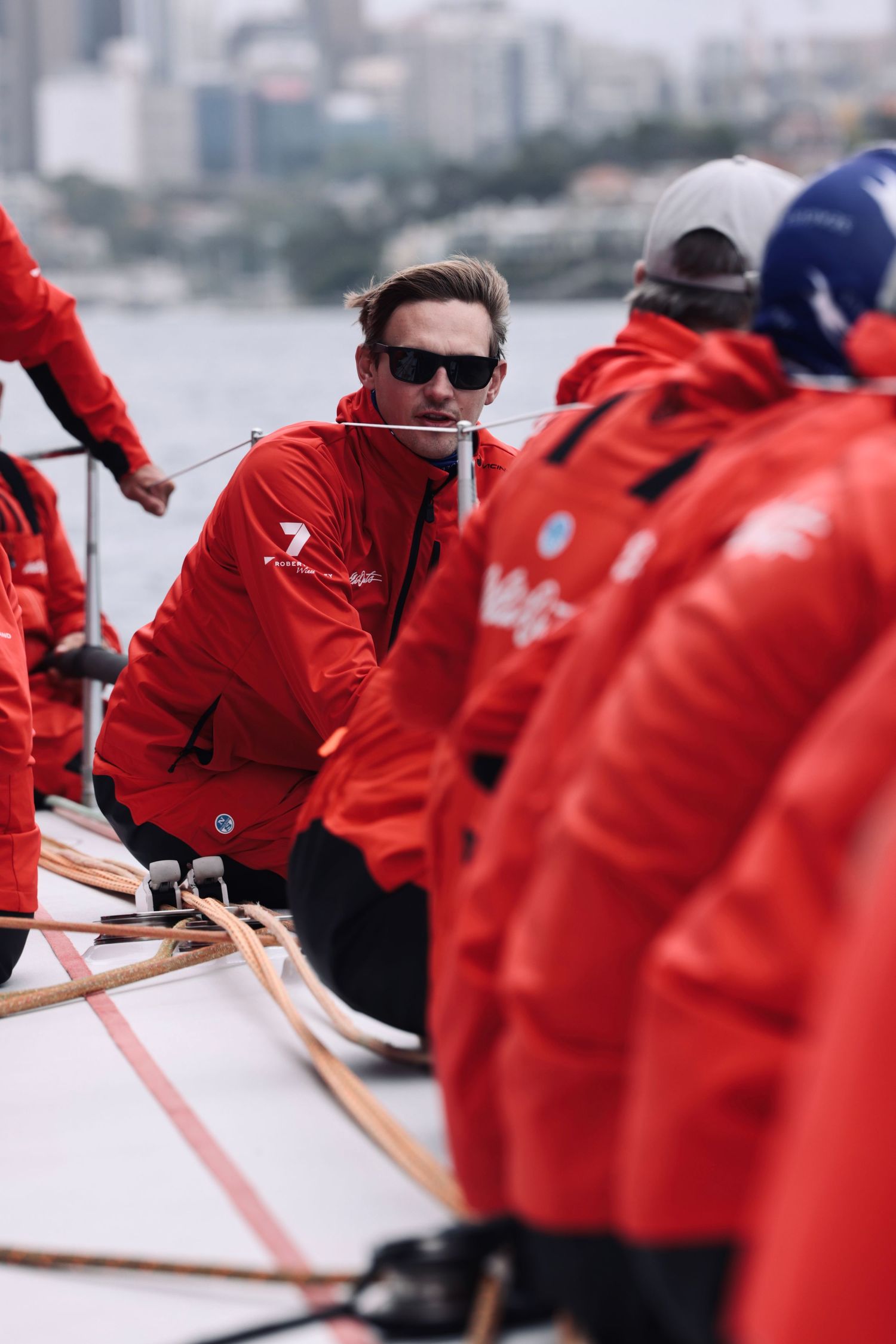 Line of sailors in red jackets working in unison aboard a racing yacht.