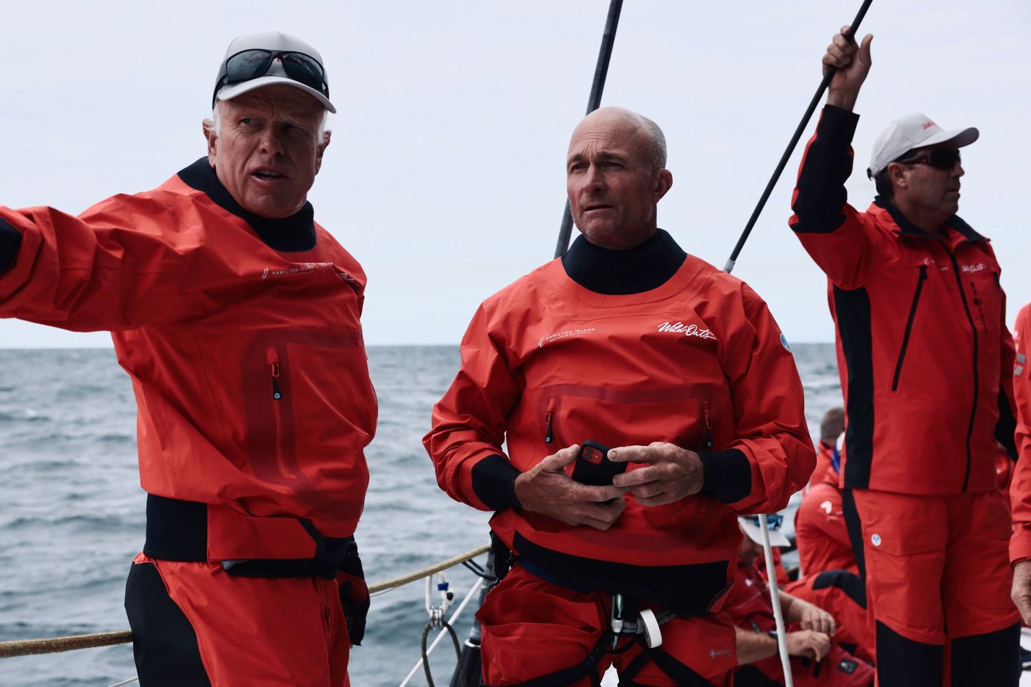 Three crew members in red sailing gear working on deck of racing yacht.