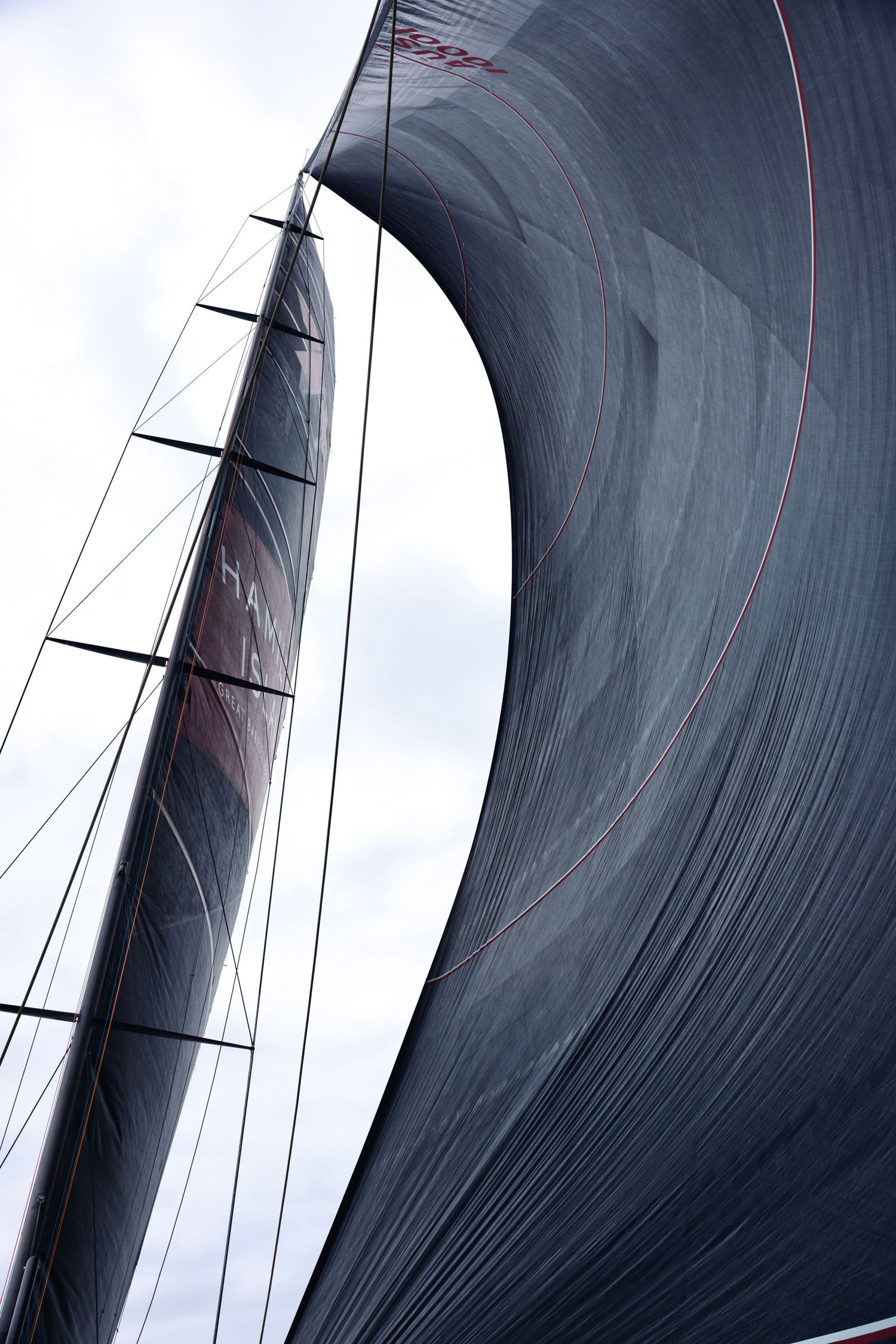 Close-up of a large black racing sail billowing against cloudy sky.