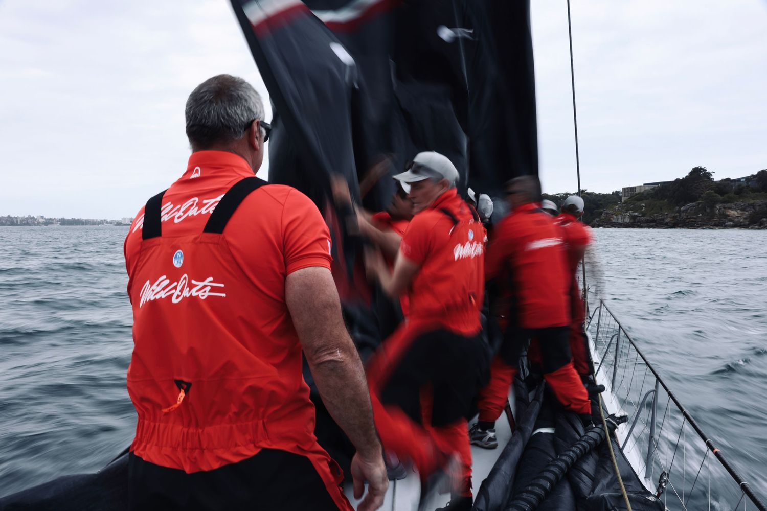 Sailing crew in red gear working on deck of a racing yacht at sea.