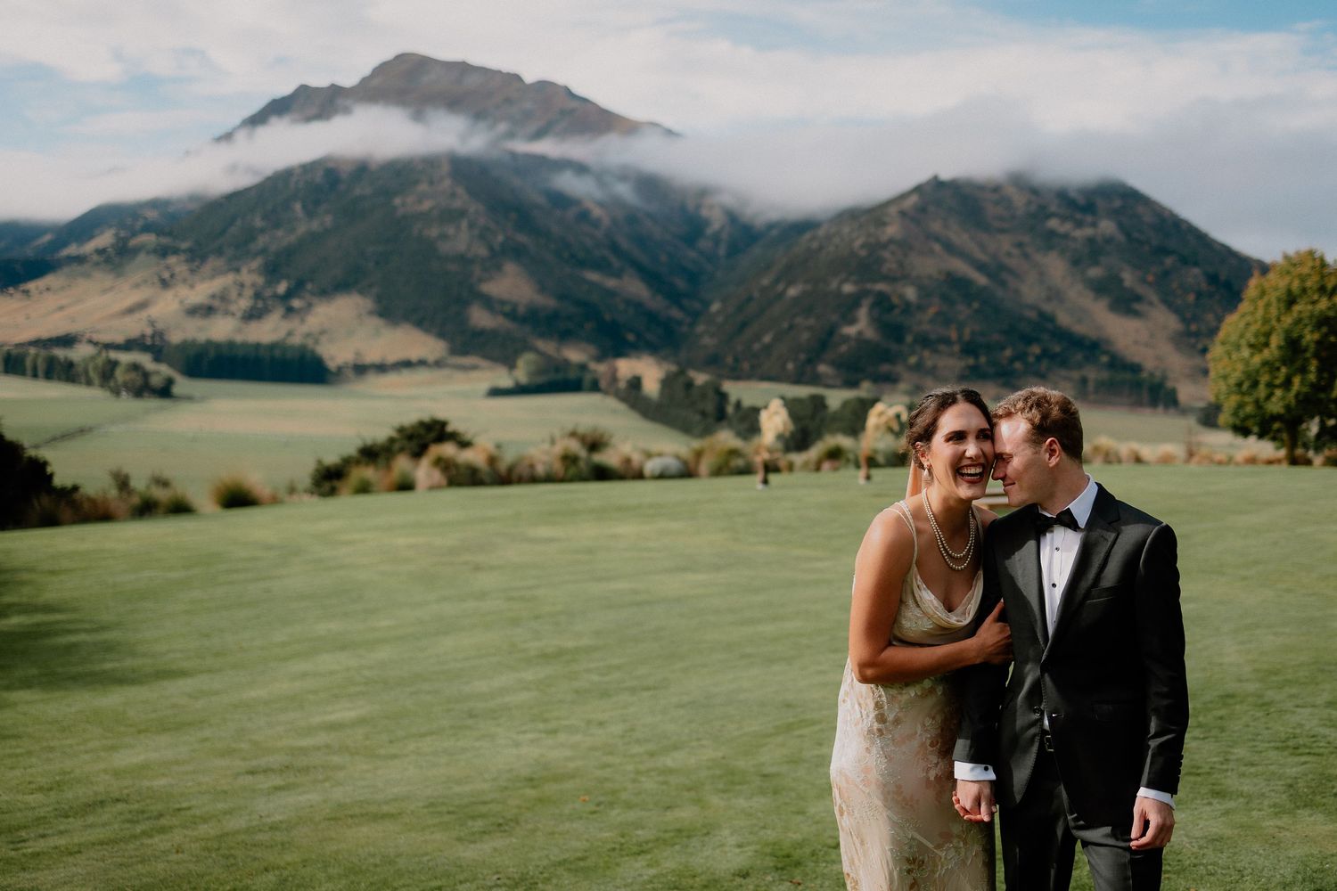 A couple embraces on a scenic hilltop overlooking rolling green mountains and valleys on their wedding day.
