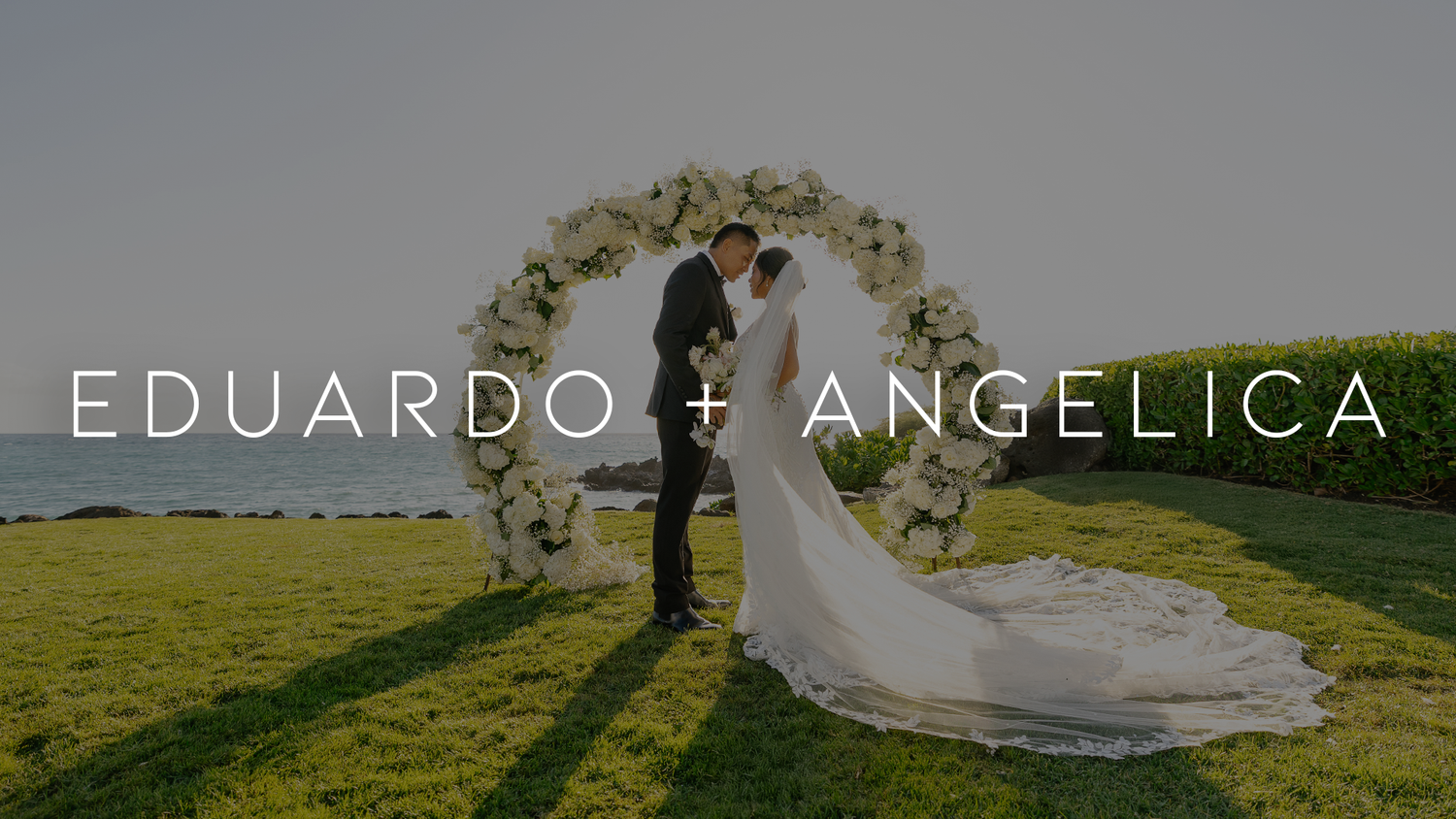 A silhouetted couple embraces under a floral arch in a scenic green field during their wedding ceremony.