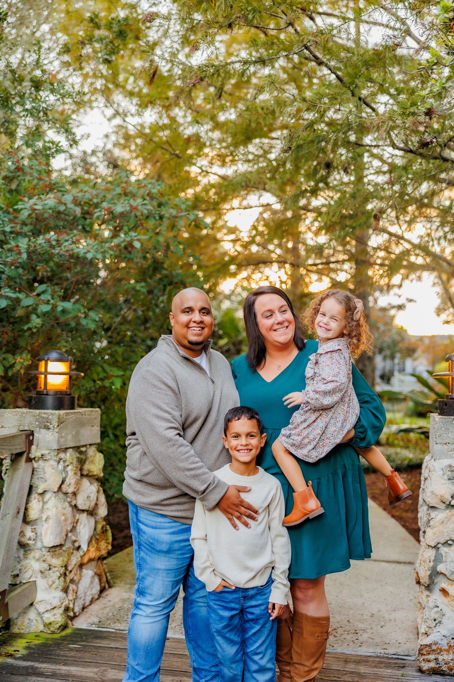 A family sits together on a wooden bench outdoors with blooming trees in the background during springtime.