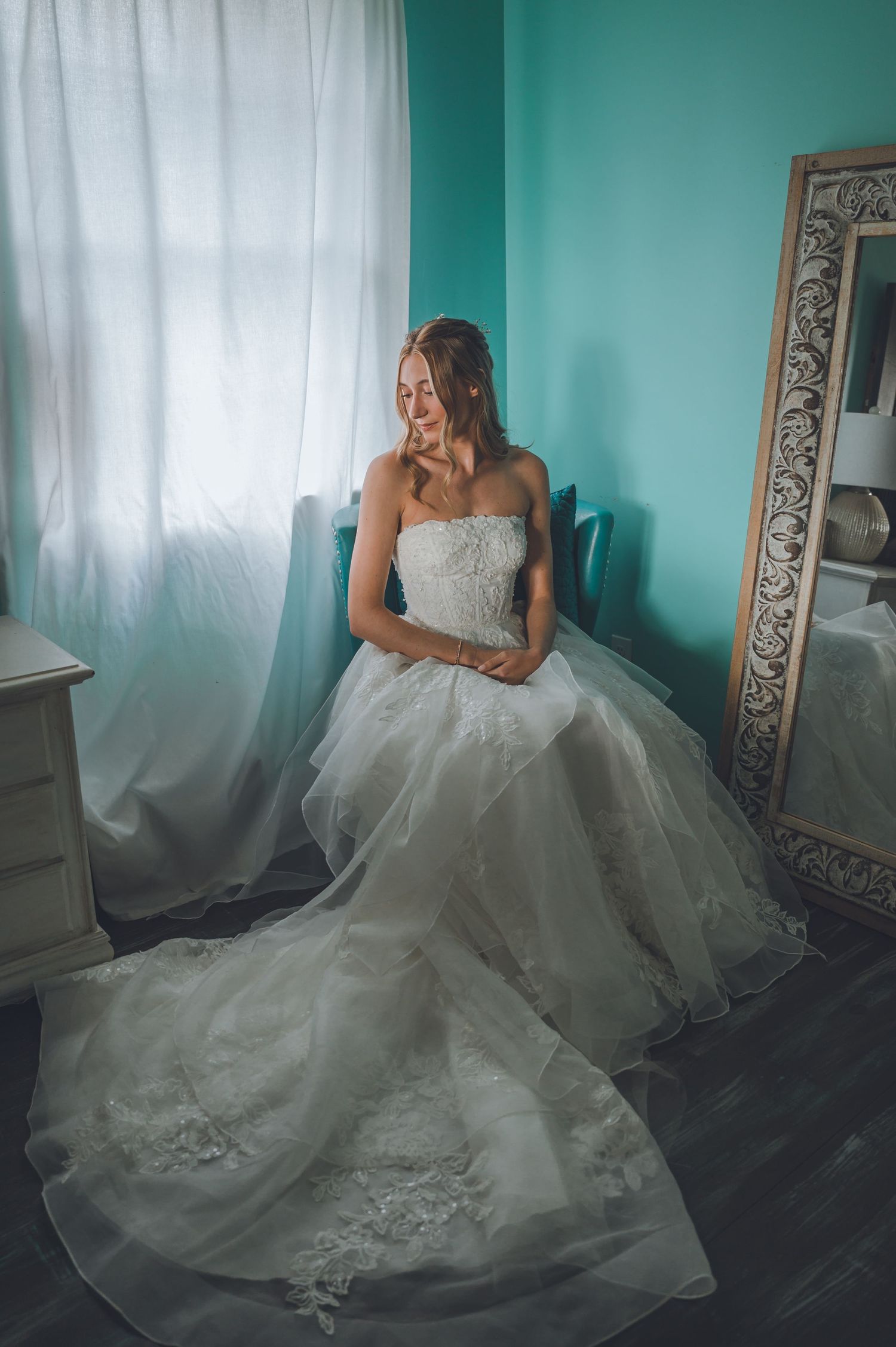 Elegant white wedding gown with intricate lace details flows across turquoise room setting.