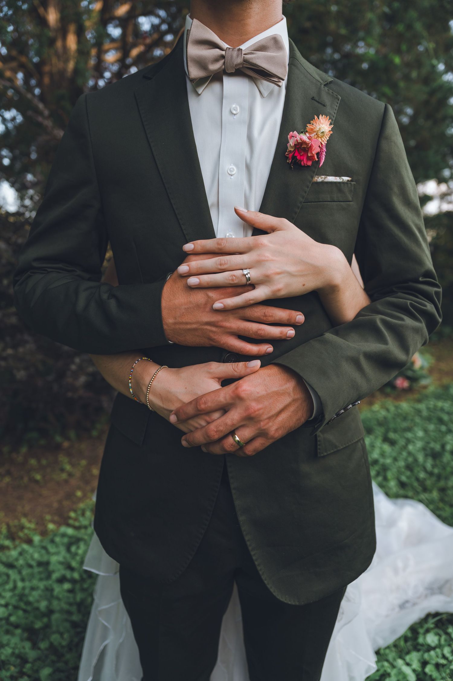 Detail shots of a groom in dark green suit with bow tie and boutonniere showing his wedding ring and hands.
