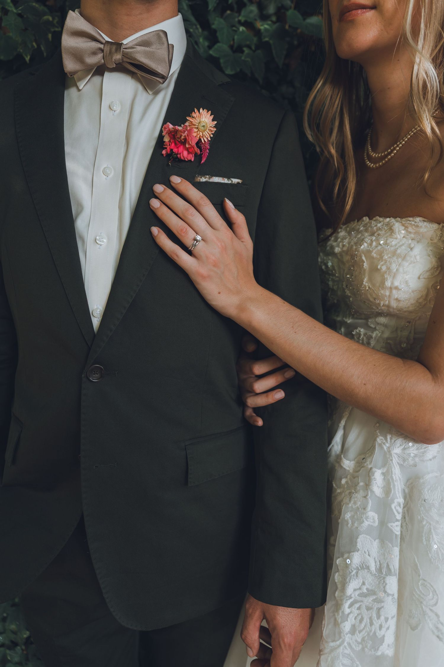 Close-up wedding photo showing bride in lace dress and groom in dark suit standing together outdoors.