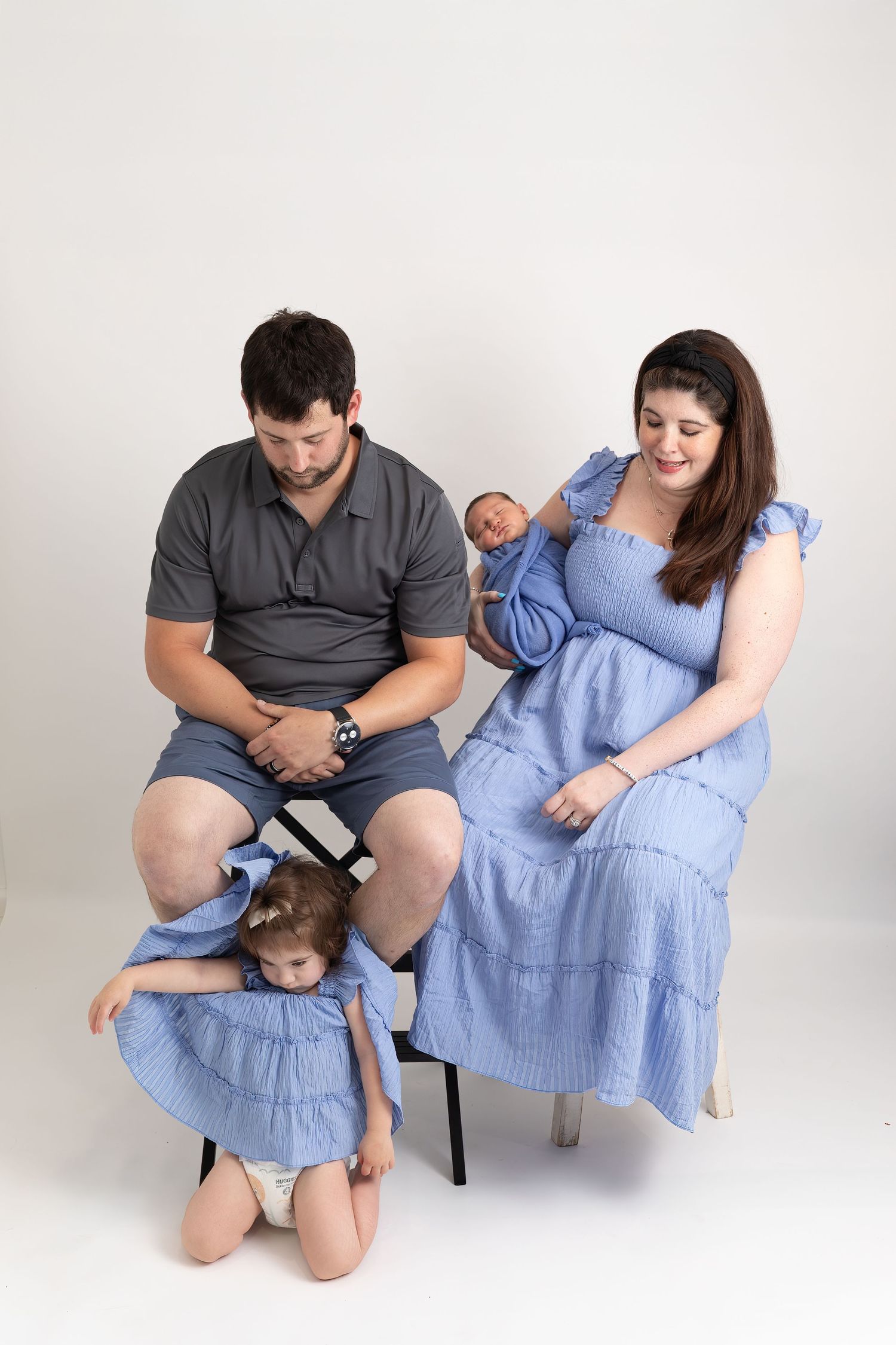 A family in coordinating blue and gray outfits poses together in a series of intimate studio portraits on a white background.