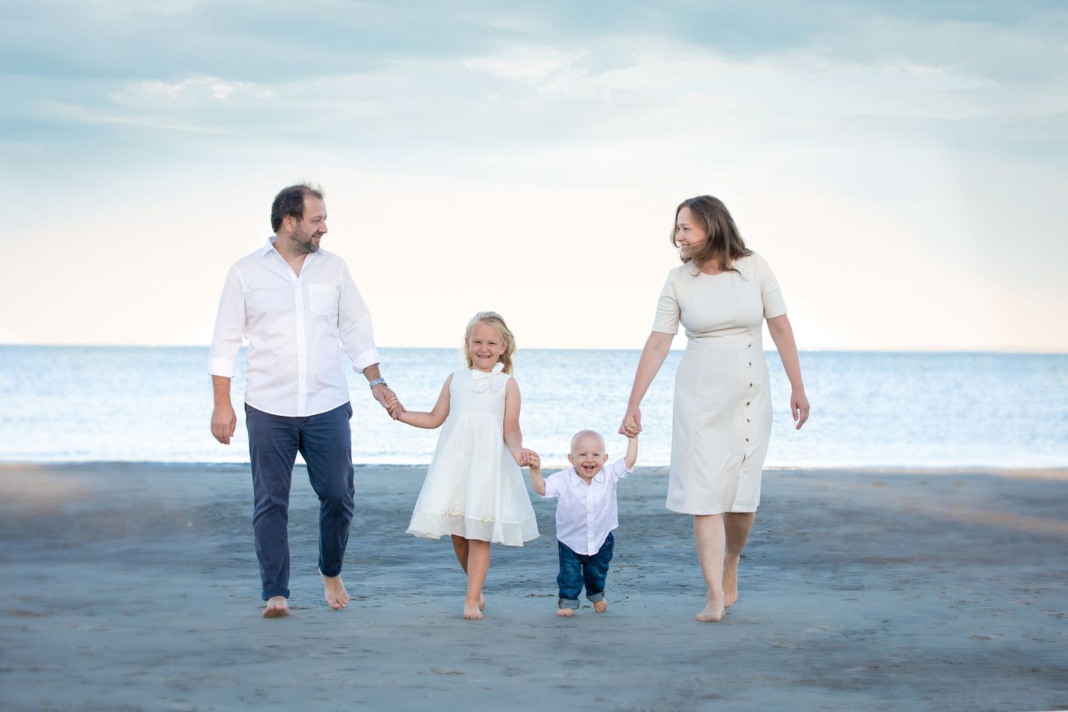 A family in white clothing walks together on a sandy beach at sunset.