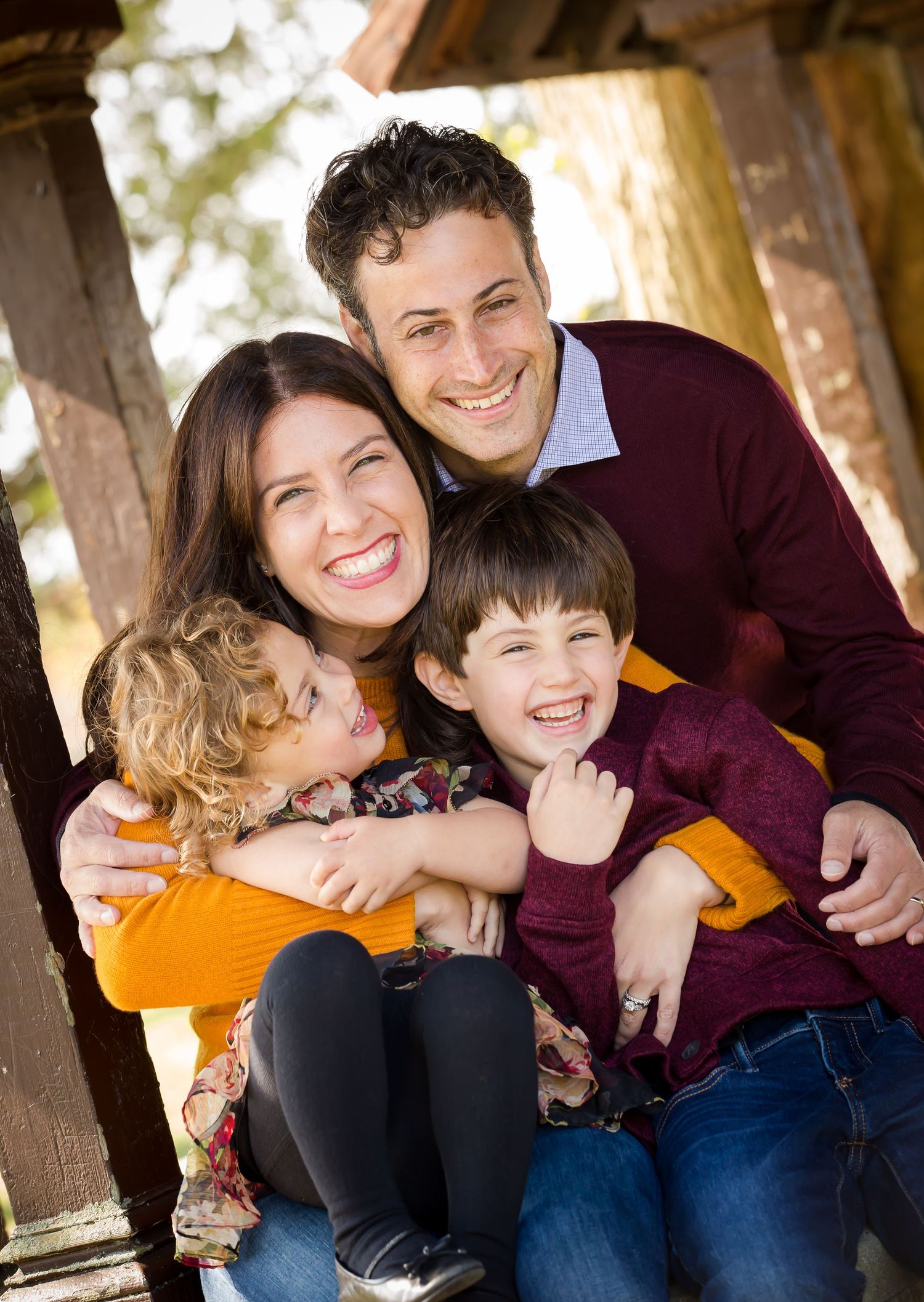A family of four shares joyful laughter while sitting together on wooden steps in an outdoor setting.