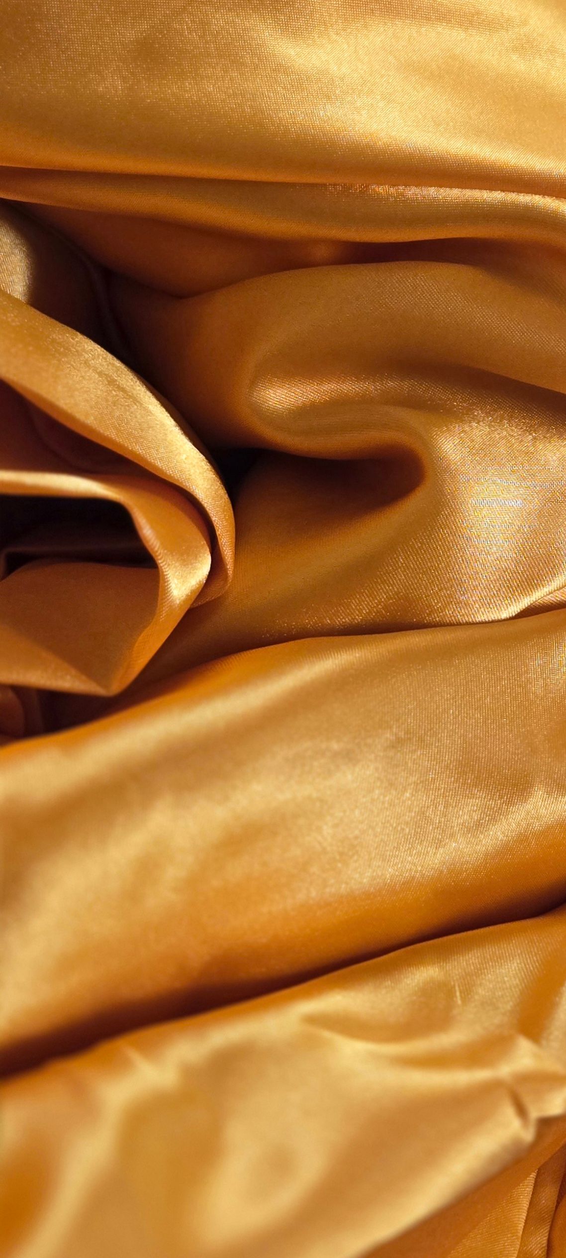 Luxurious golden silk fabric draped in elegant folds showing smooth texture and warm metallic sheen.