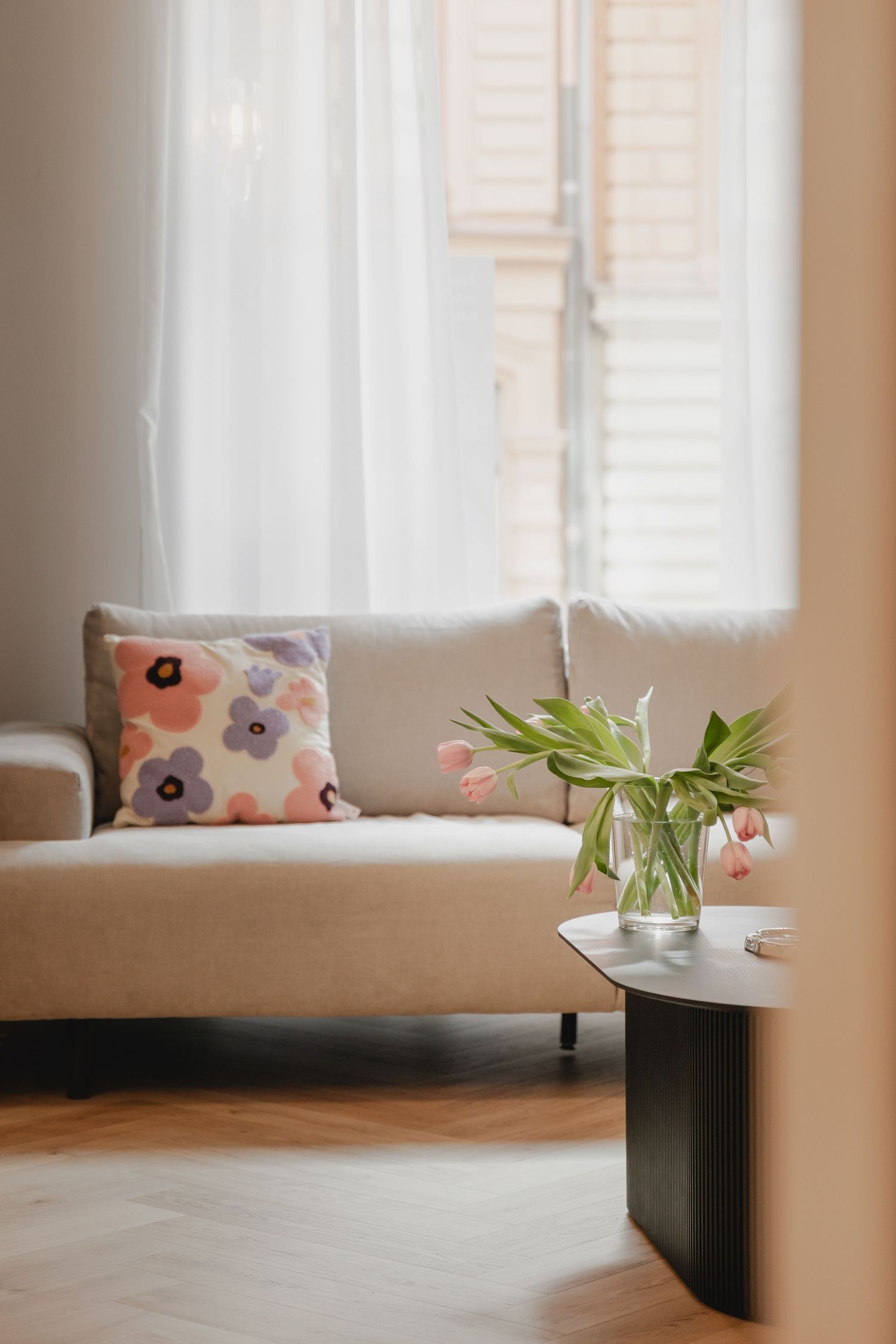 Studio Michelles väntrum, detaljbild på soffa med blommig kudde och rosa tulpaner i förgrunden. Skira gardiner i bakgrunden