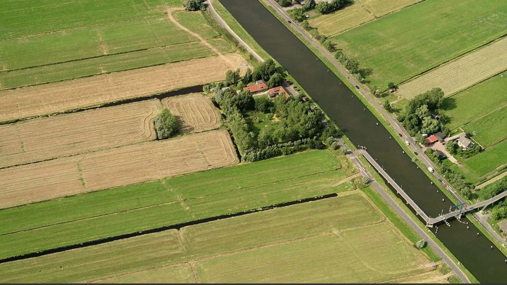 Aerial view of a rural canal cutting through green agricultural fields with farmland and trees along its banks.
