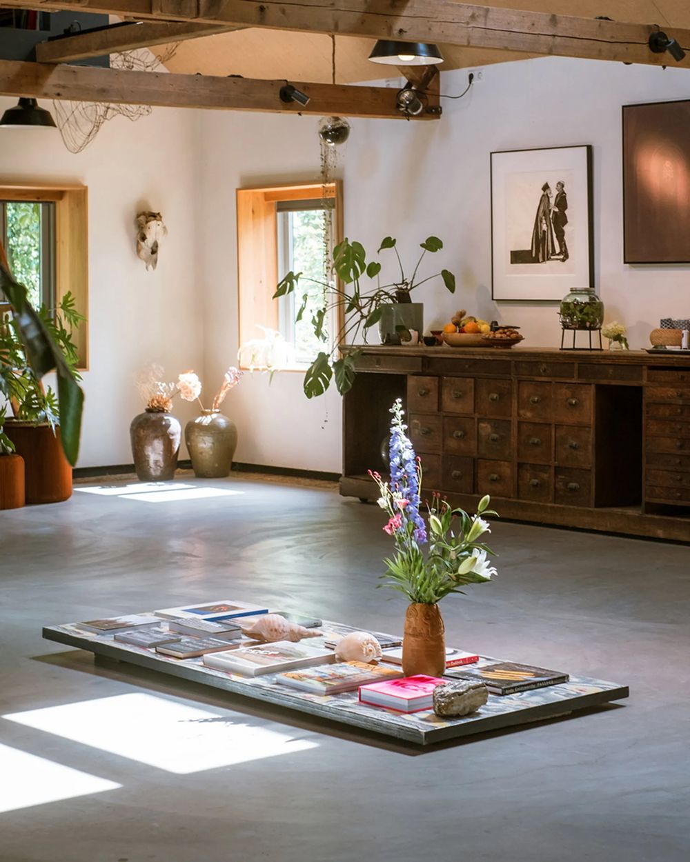 A sequence of four interior gallery spaces showing a minimalist exhibition setup with wooden furniture and natural light.