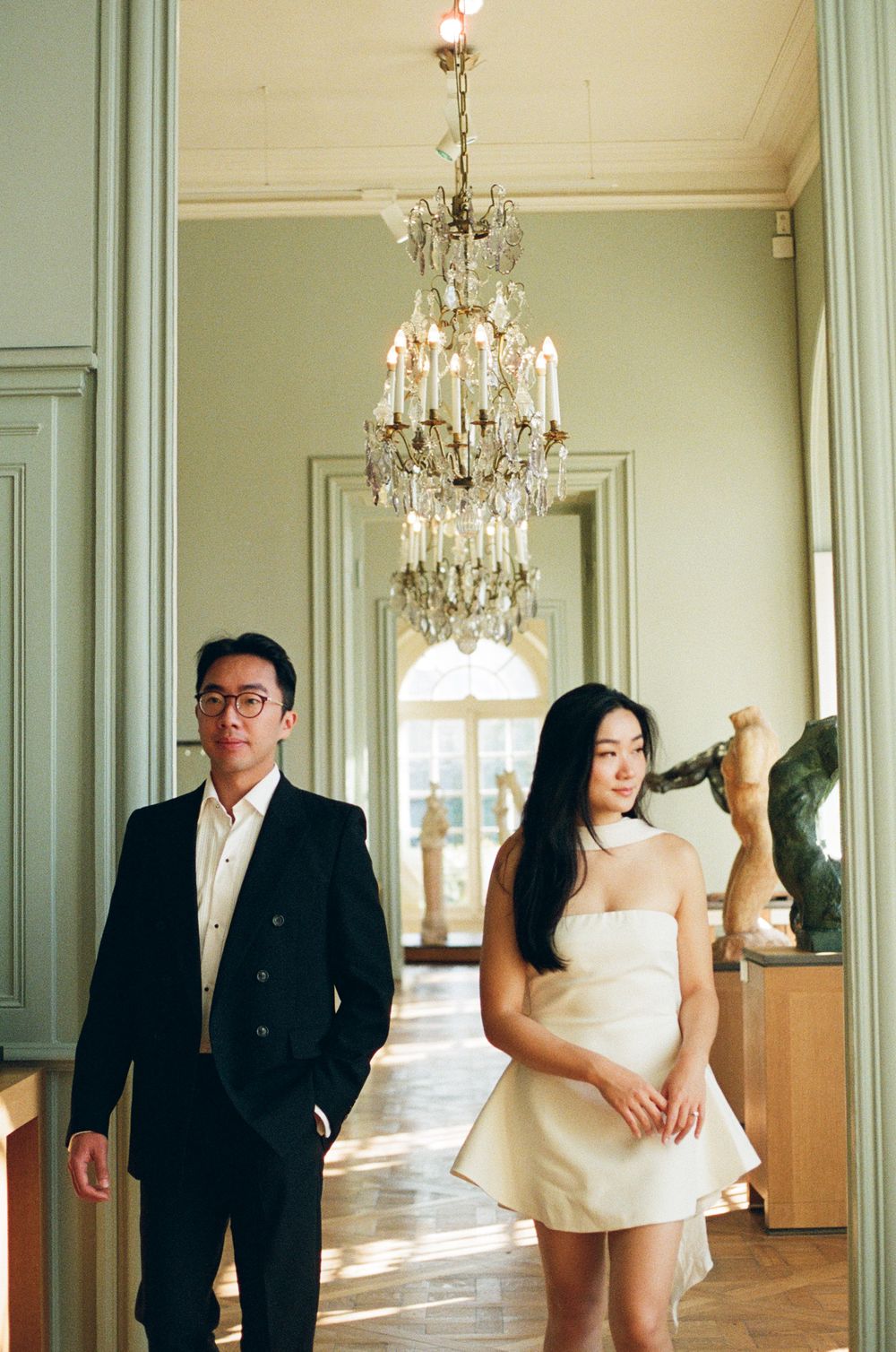 Elegant wedding couple poses in a grand hall with crystal chandeliers and mint green walls.