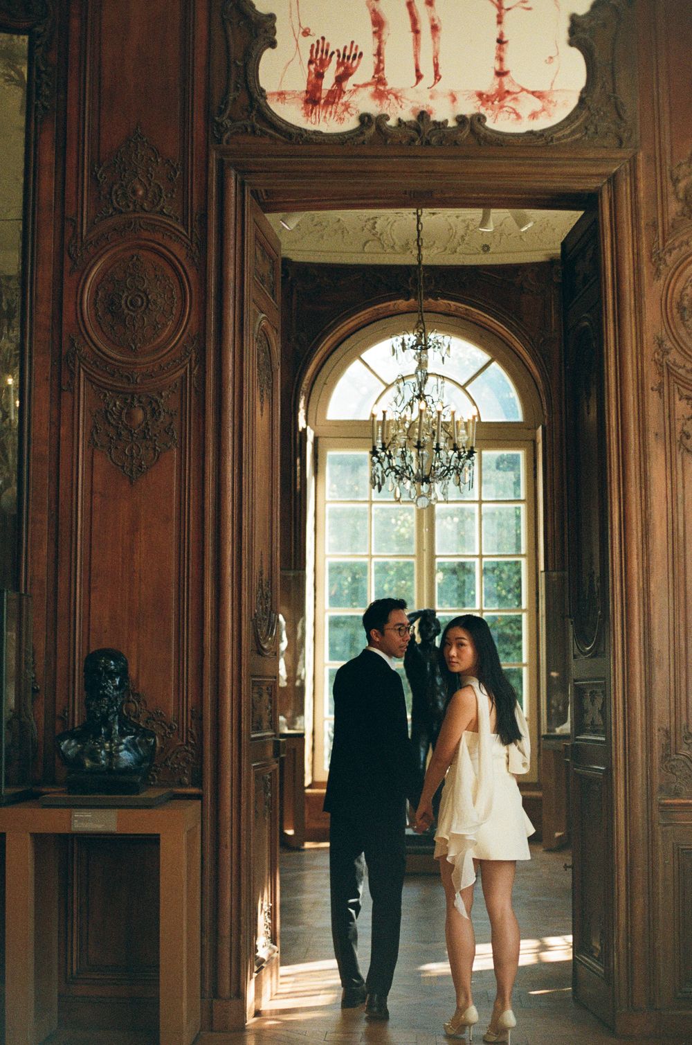 Couple poses playfully in an elegant wood-paneled room with arched windows and ornate details.