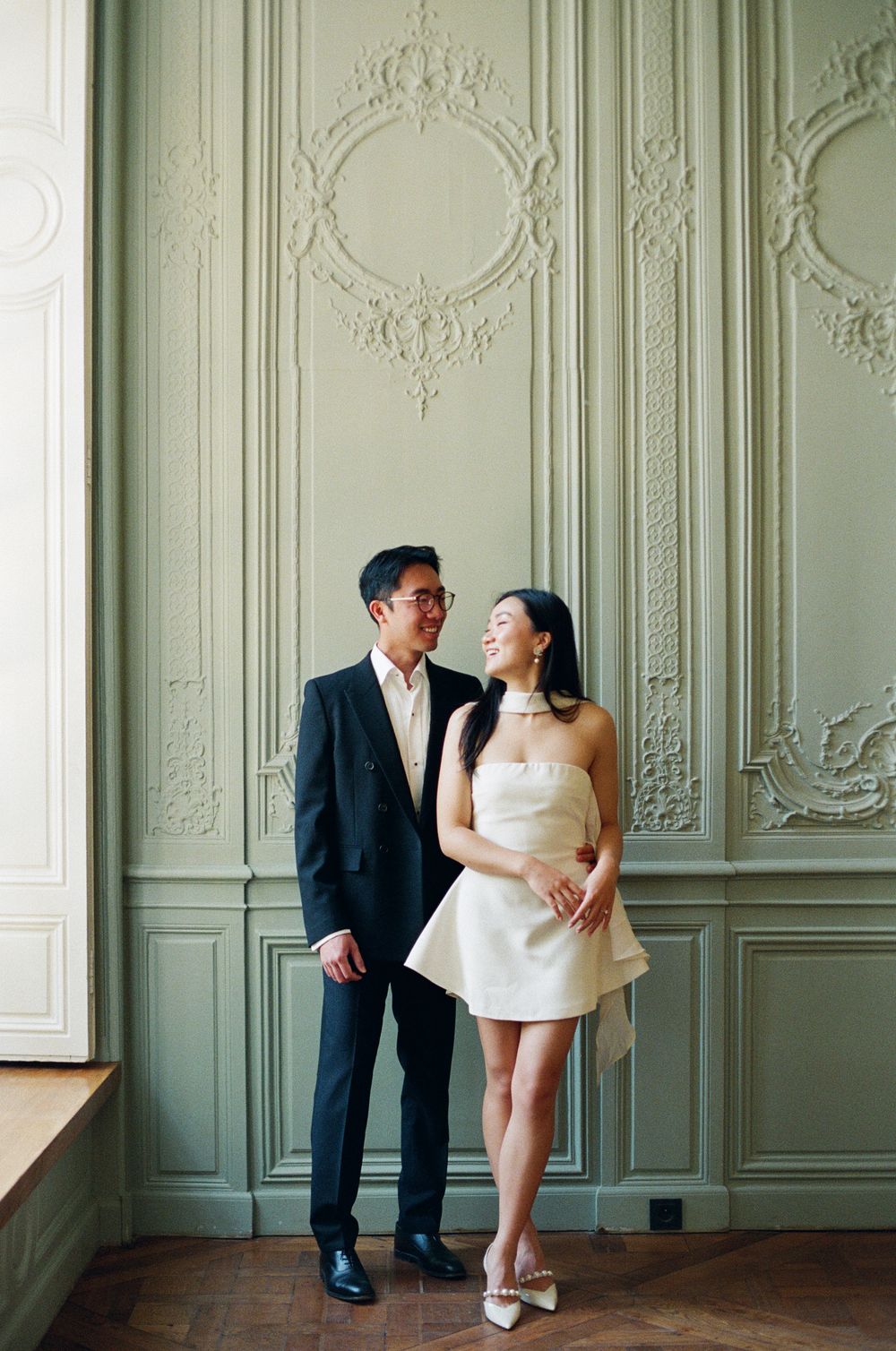 Romantic couple shares a tender moment against ornate white wall panels in a vintage interior. Musee Rodin photoshoot.