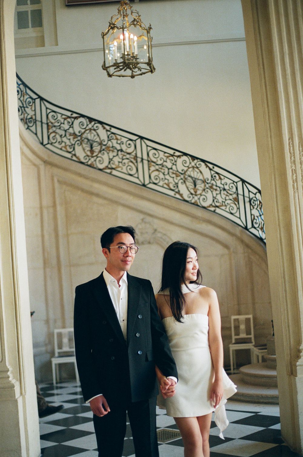 Couple laughing together in a grand hallway with elegant staircase and chandelier. Musee Rodin photoshoot.