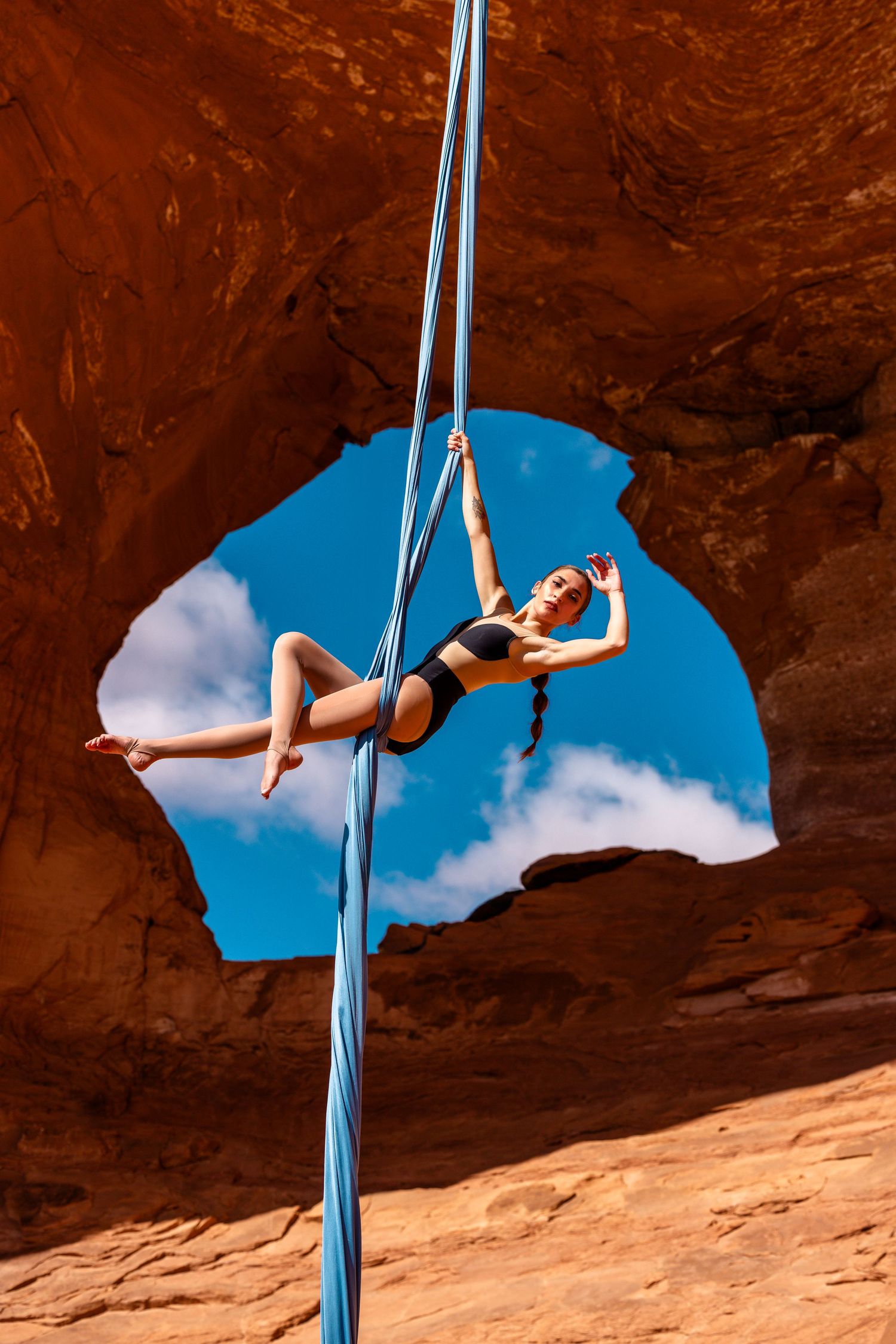 Aerialist on silks in front of a towering Utah red rock arch; polished aerial arts image blending strength, lines, and landscape.