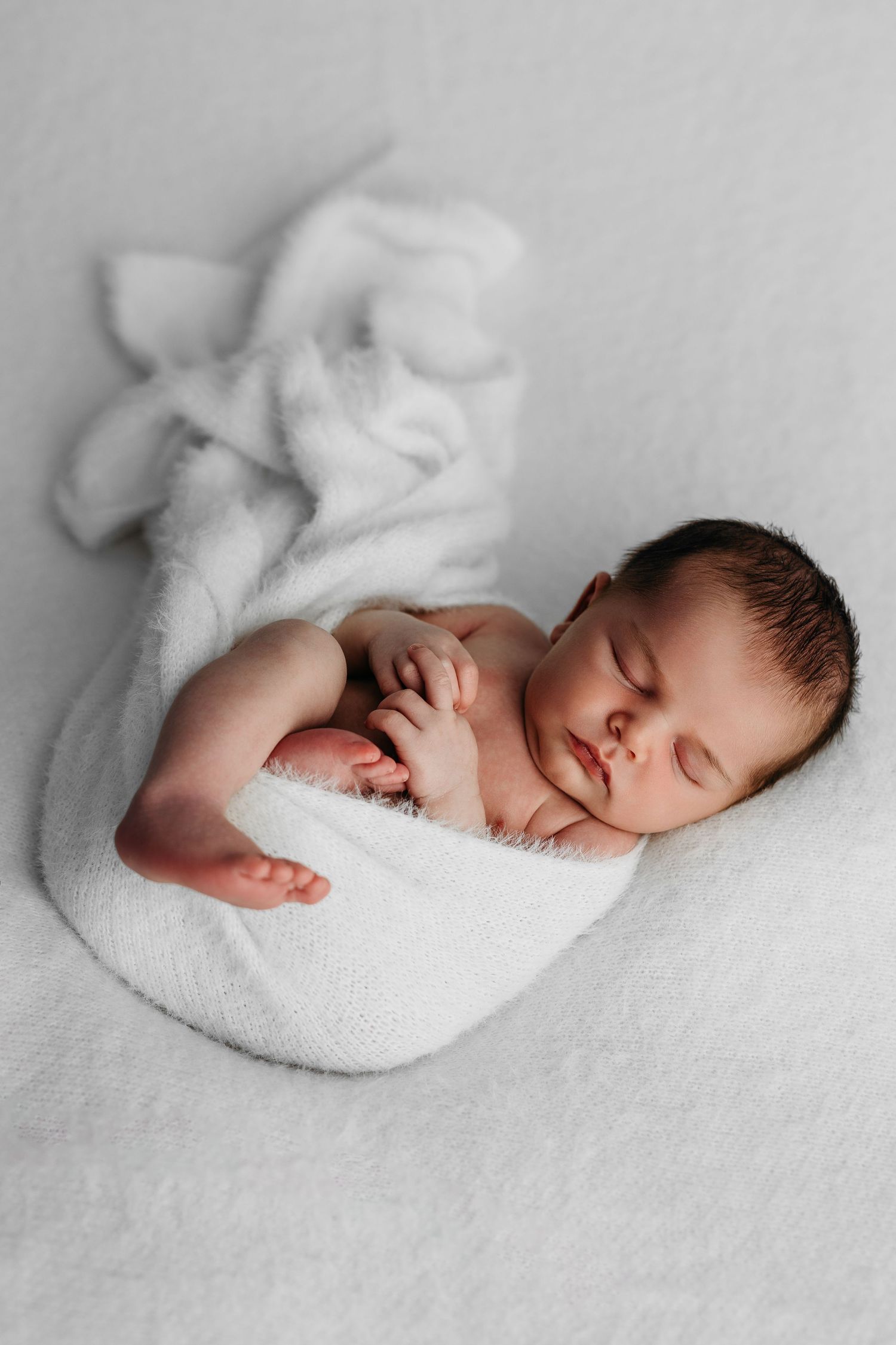 Peaceful newborn baby sleeping wrapped in soft white blanket during professional photography session.