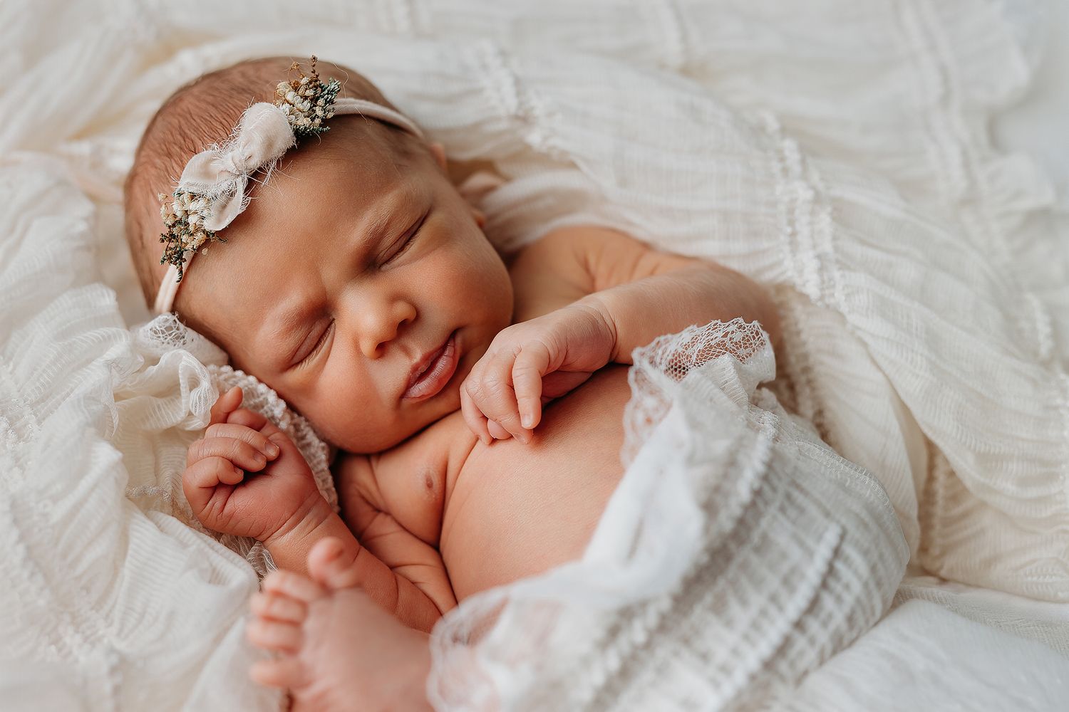 Peaceful newborn baby sleeping wrapped in soft white blanket during professional photography session.