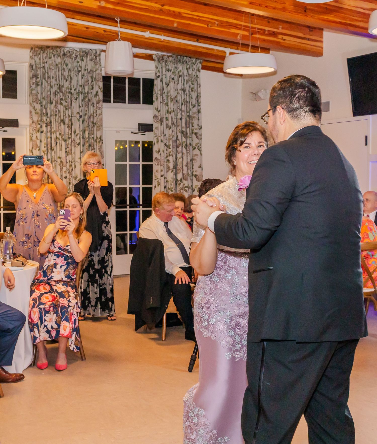 Couples dancing and socializing at an elegant indoor venue with exposed wooden beams and white curtains.