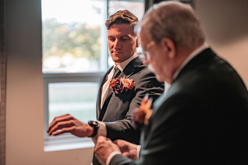 Men in formal attire adjusting their suits by a waterfront setting.