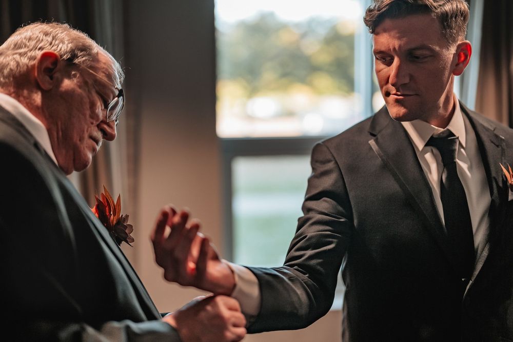 Groom prepares for wedding day while looking out window.