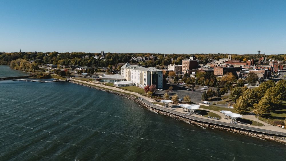 Panoramic aerial view of a waterfront cityscape with buildings and shoreline on a clear blue day.