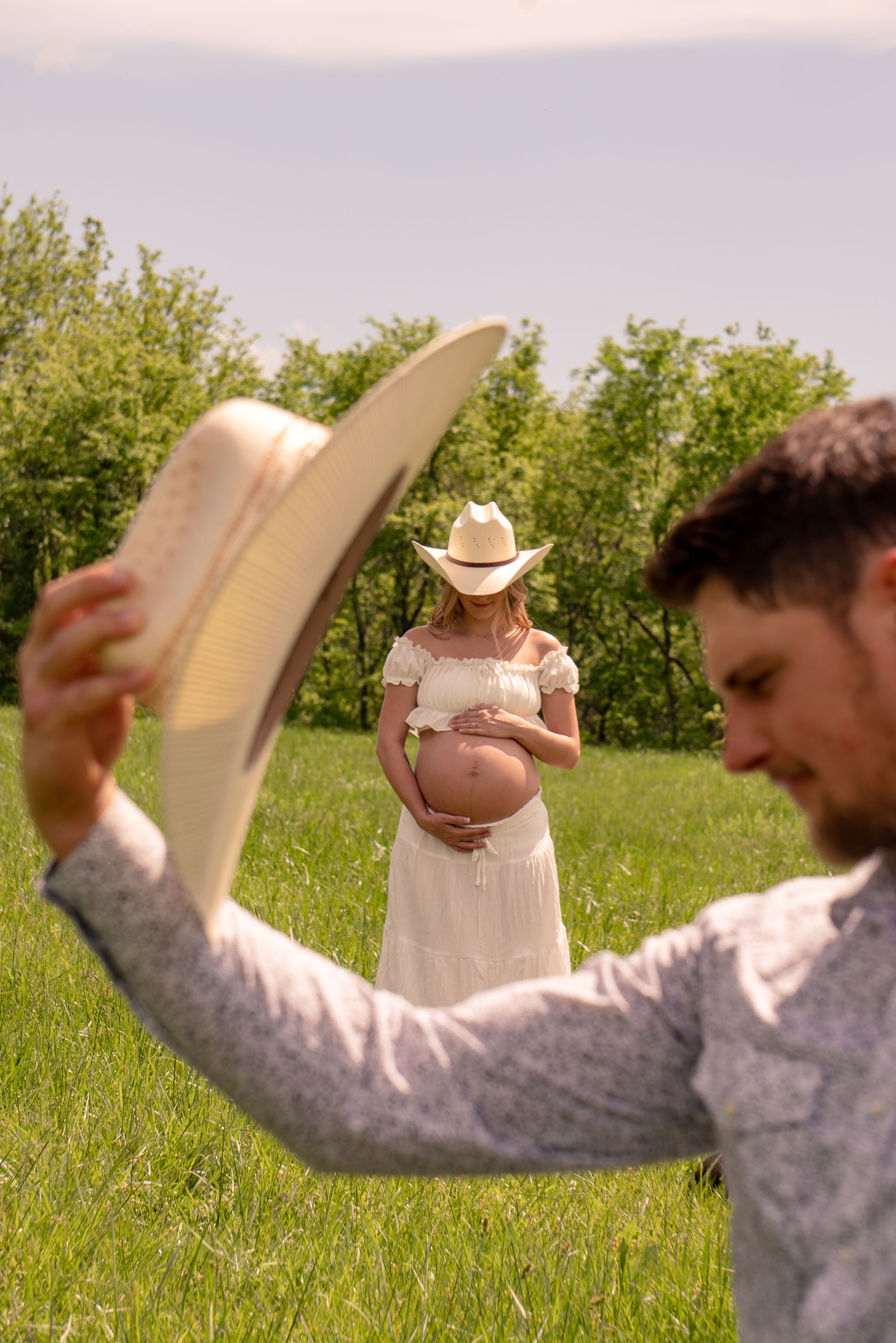 A couple, the lady is standing in the middle ground  in focus while her husband frames around her with his side profile and hat.