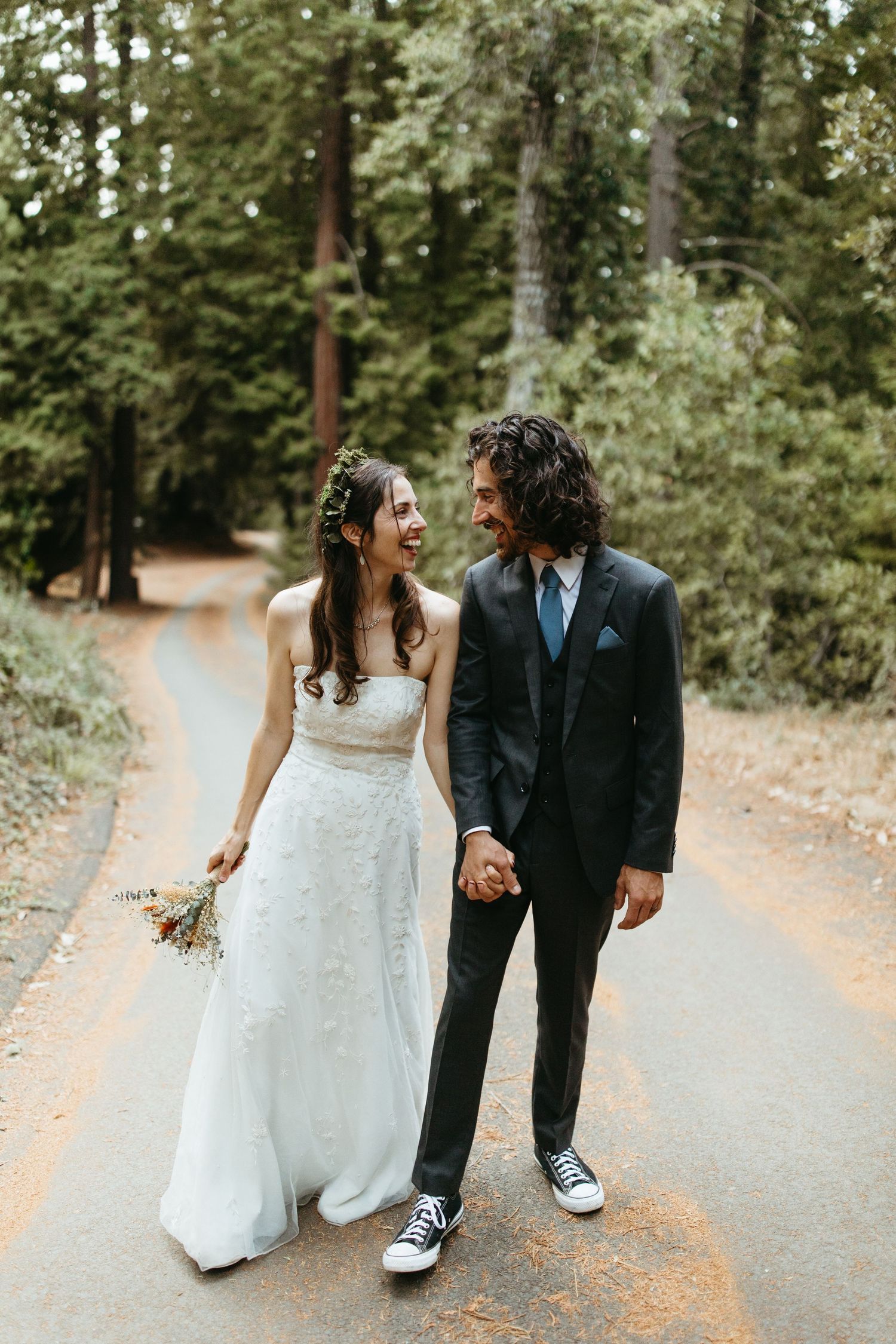 Casual wedding couple walking and laughing together on forest path wearing sneakers.
