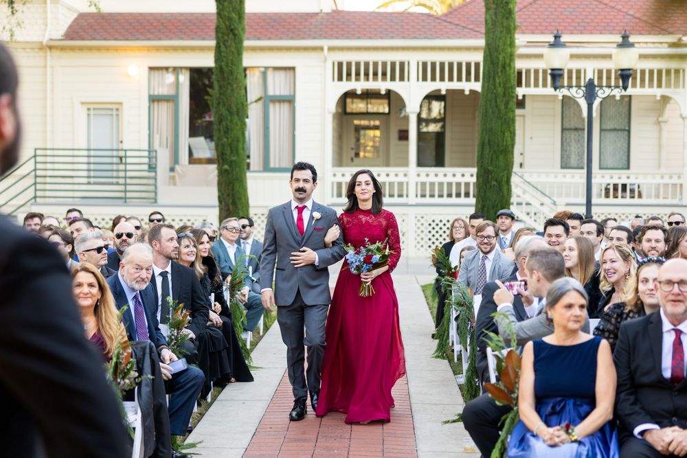 Wedding party members walk along a covered outdoor walkway with white columns and red roof tiles.