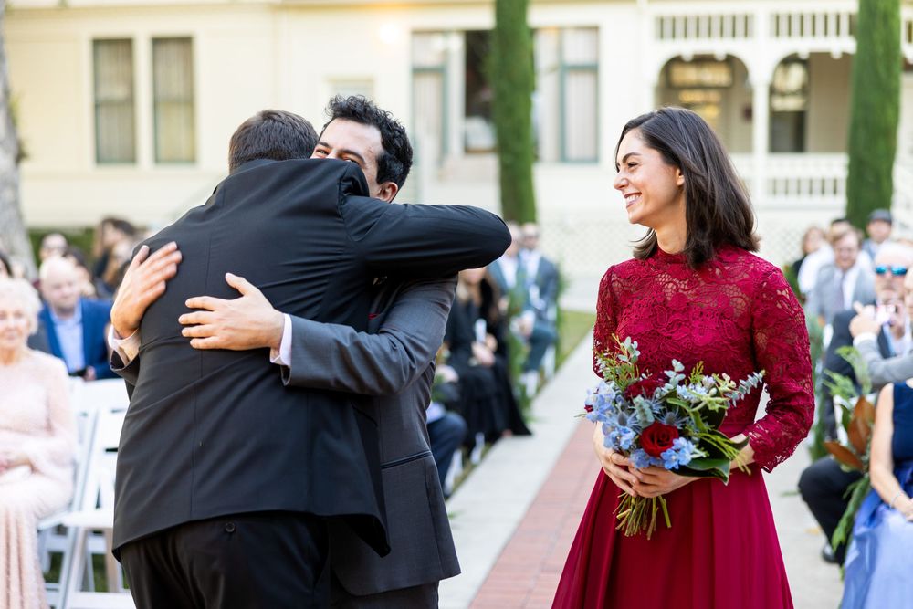 Wedding guests dance and celebrate during an outdoor reception with tables and chairs visible in the background.