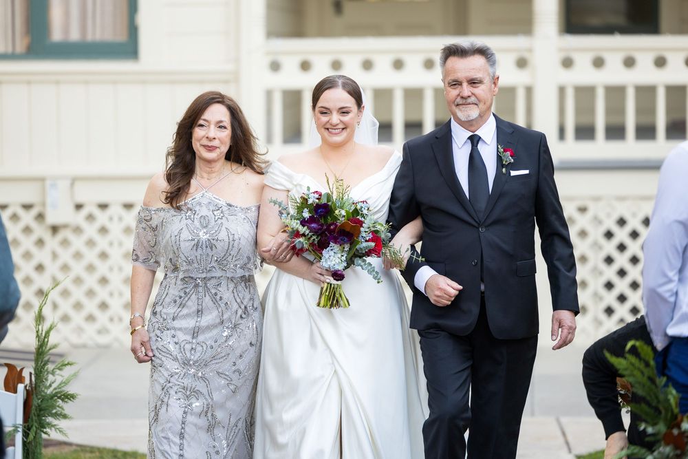 Wedding processional with bridesmaids in silver dresses walking down an outdoor path.