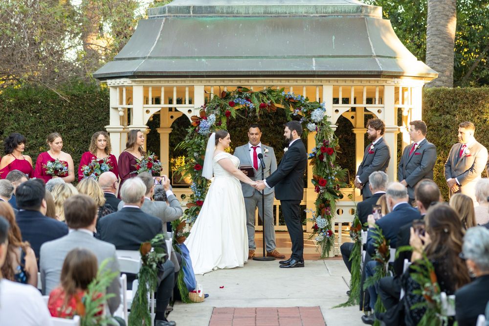 Outdoor wedding ceremony setup with white chairs and gazebo surrounded by palm trees.