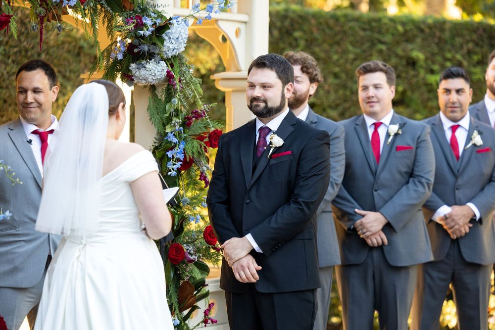 Wedding party stands together outdoors under golden sunlight with floral decorations and trees in the background.
