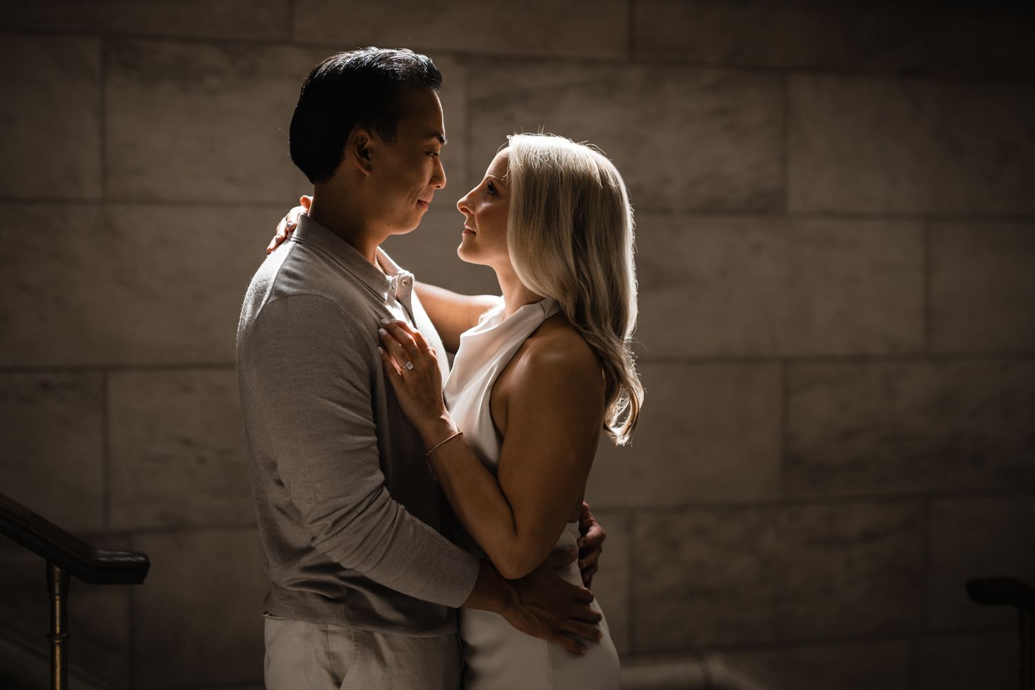 Romantic couple embracing in moody lighting against stone wall backdrop.