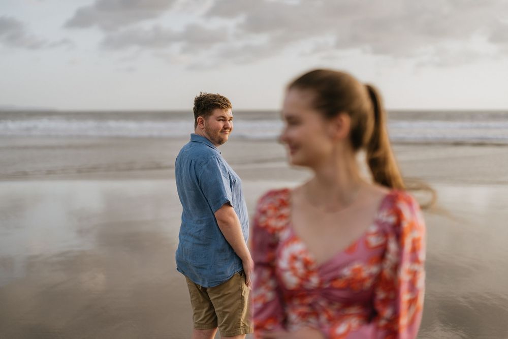 A couple shares a candid moment together on a cloudy beach with soft focus in the foreground.