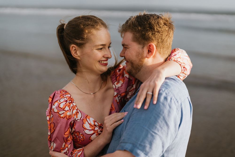 A joyful couple shares an intimate moment while laughing together on a beach at dusk.