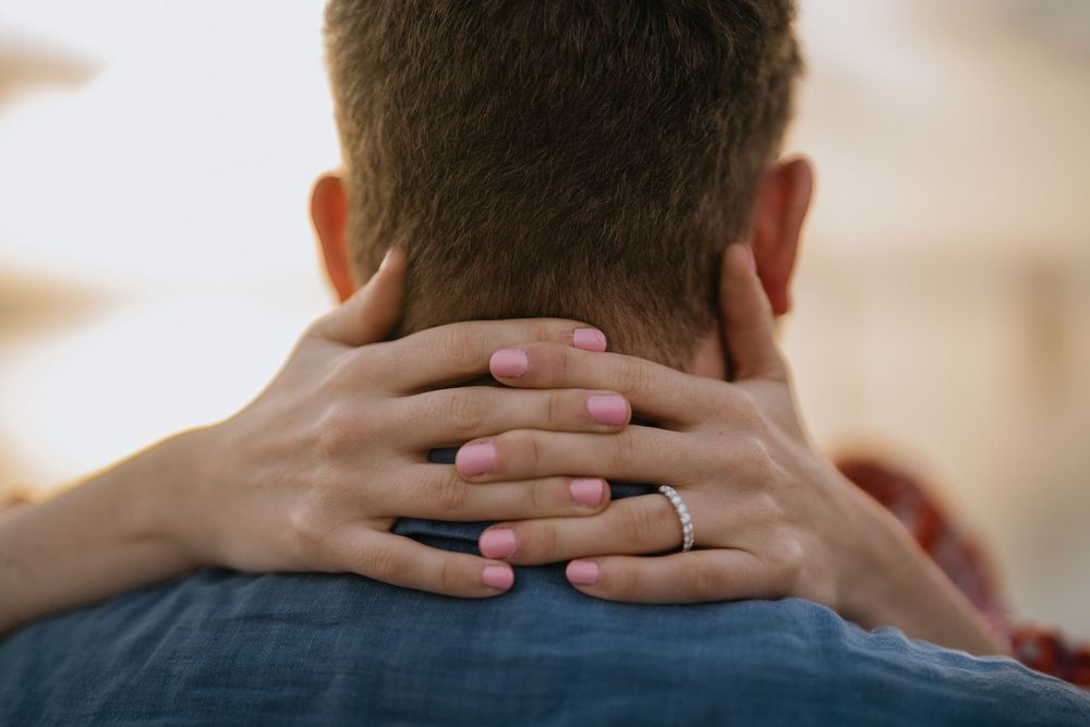 Close-up view of hands tenderly touching the back of a neck in an intimate moment.