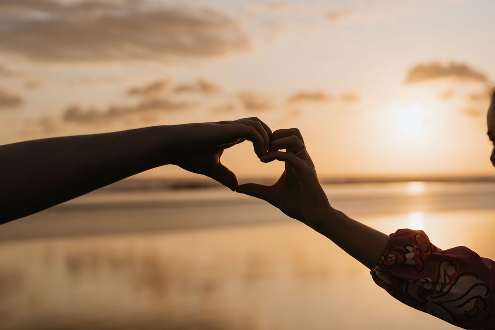 A hand silhouetted against a golden sunset sky gestures toward the glowing sun on the horizon.