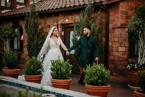 A couple walks hand in hand by a pool at a rustic Spanish-style venue.