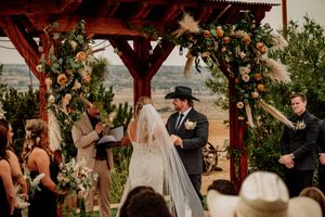 Wedding ceremony under wooden pergola decorated with lush florals and greenery at sunset.