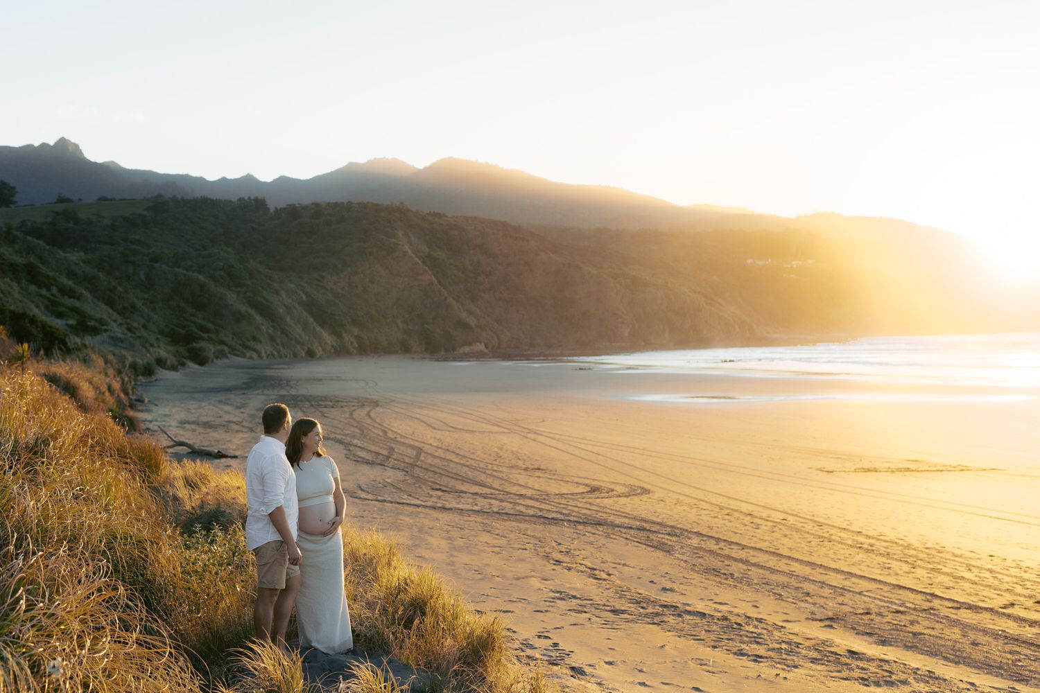 Couple walking along scenic coastal path during golden sunset over rugged beach landscape.